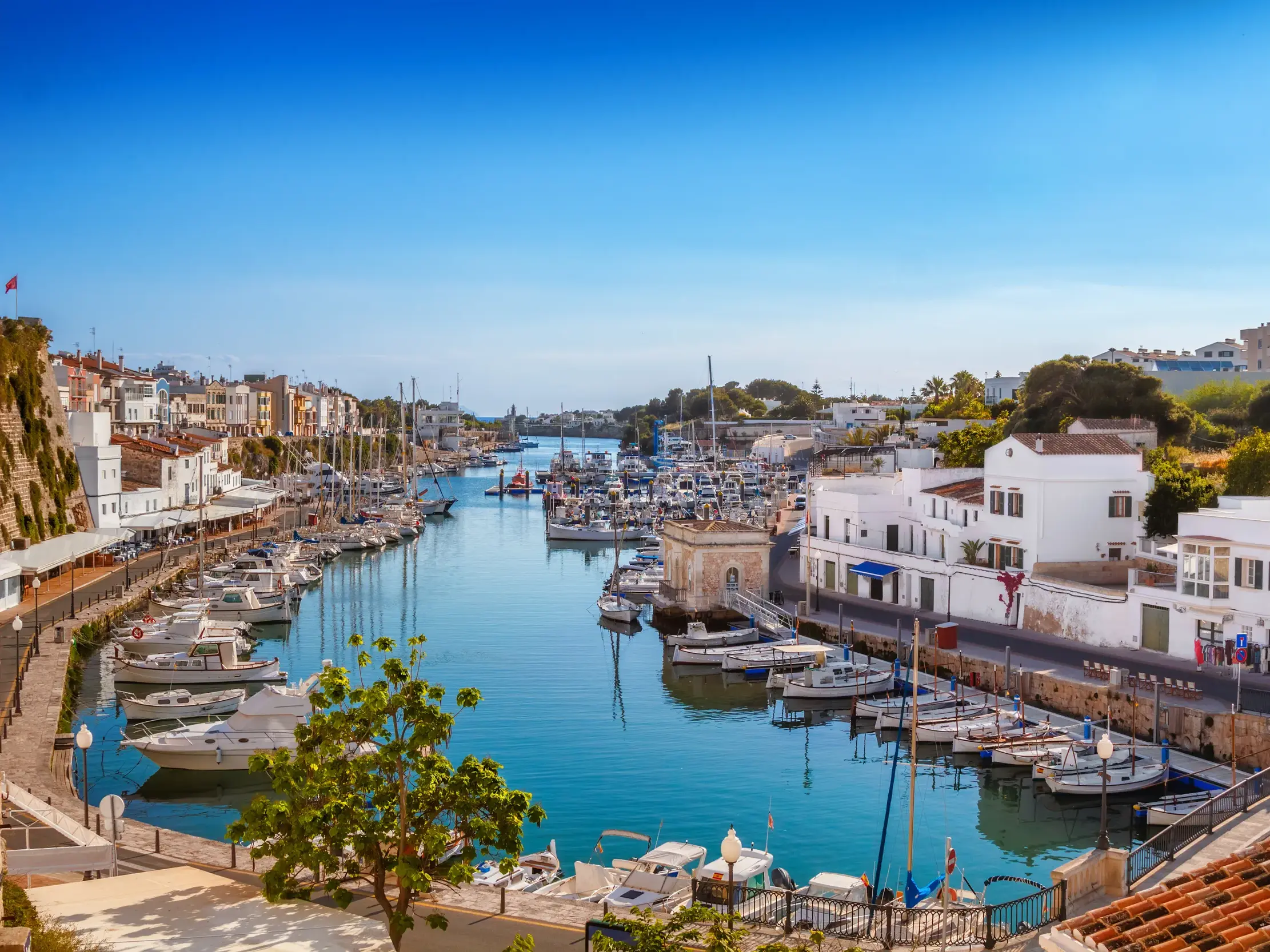 Malerischer Hafen von Ciutadella auf Menorca an einem sonnigen Tag mit vielen Booten und historischen Häusern am Ufer.