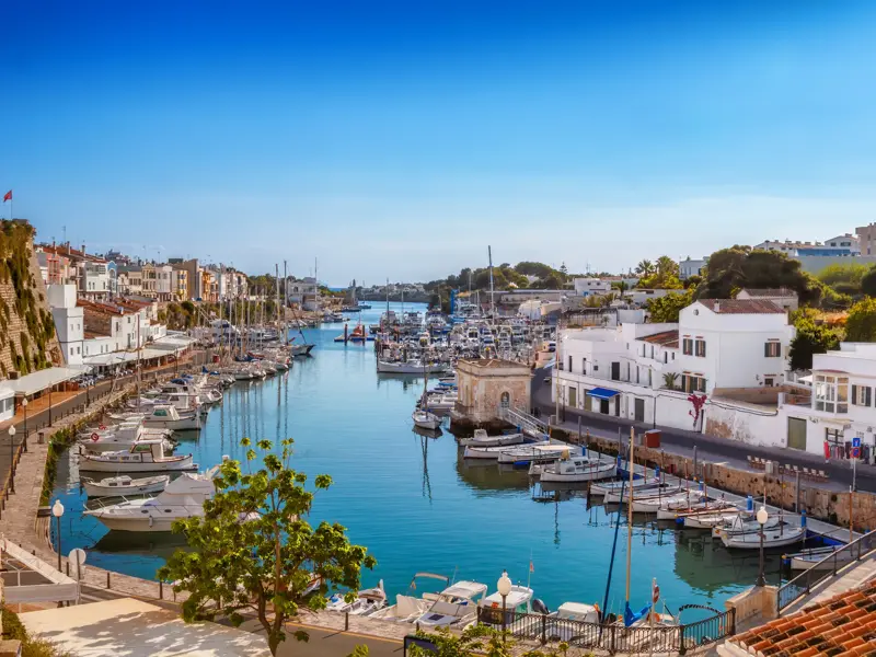 Malerischer Hafen von Ciutadella auf Menorca an einem sonnigen Tag mit vielen Booten und historischen Häusern am Ufer.