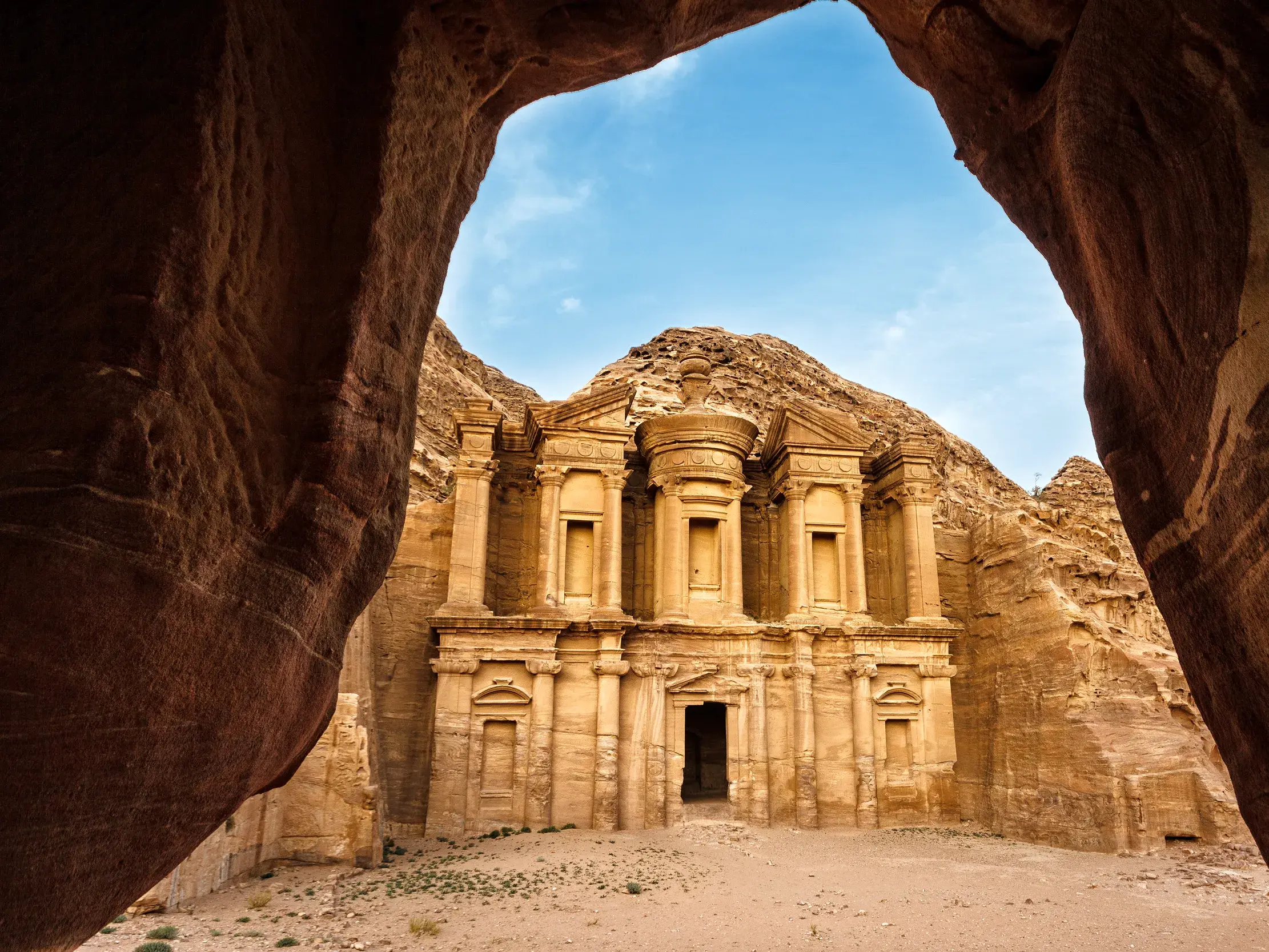 Blick durch eine Höhle auf das Kloster Ad-Deir in der Felsenstadt Petra, ein Highlight einer Gruppenreise durch Jordanien.