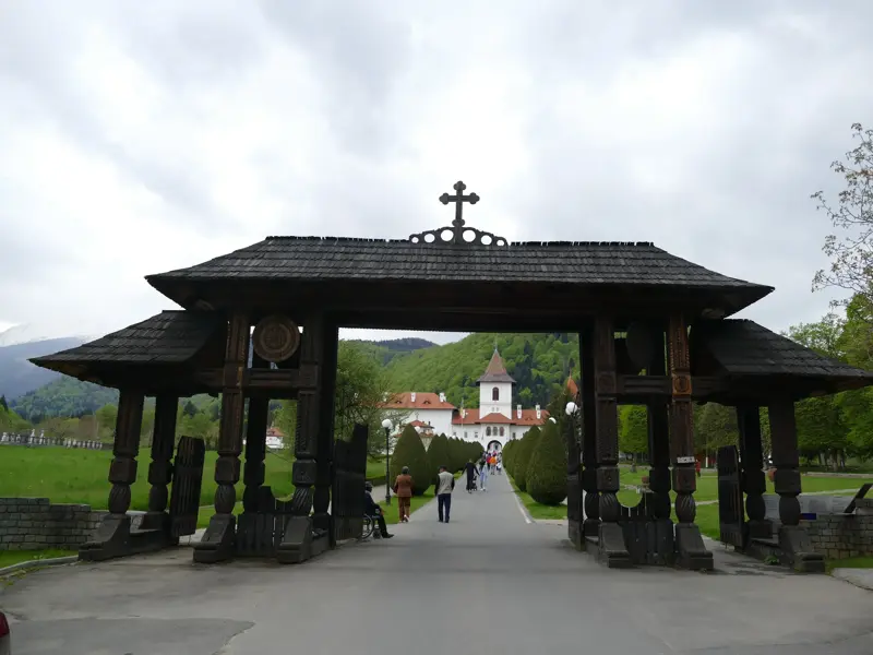 Traditionelles, geschnitztes Holztor am Eingang zum orthodoxen Sambata-Kloster vor der Kulisse der bewaldeten Karpaten.