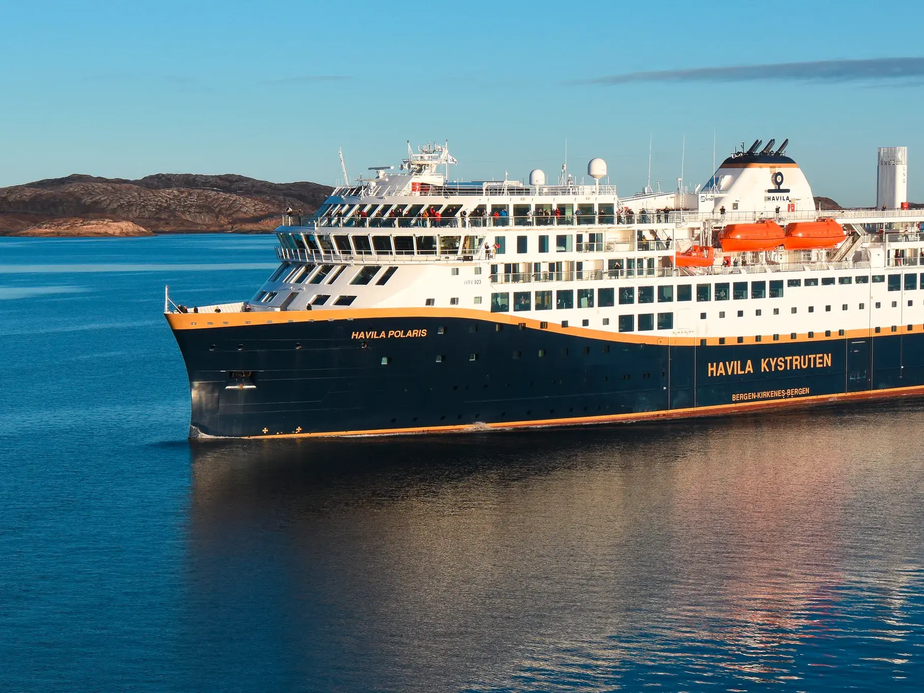 Das moderne Postschiff Havila Polaris gleitet auf einer Studienreise durch das ruhige, blaue Meer entlang der felsigen Küste Norwegens.