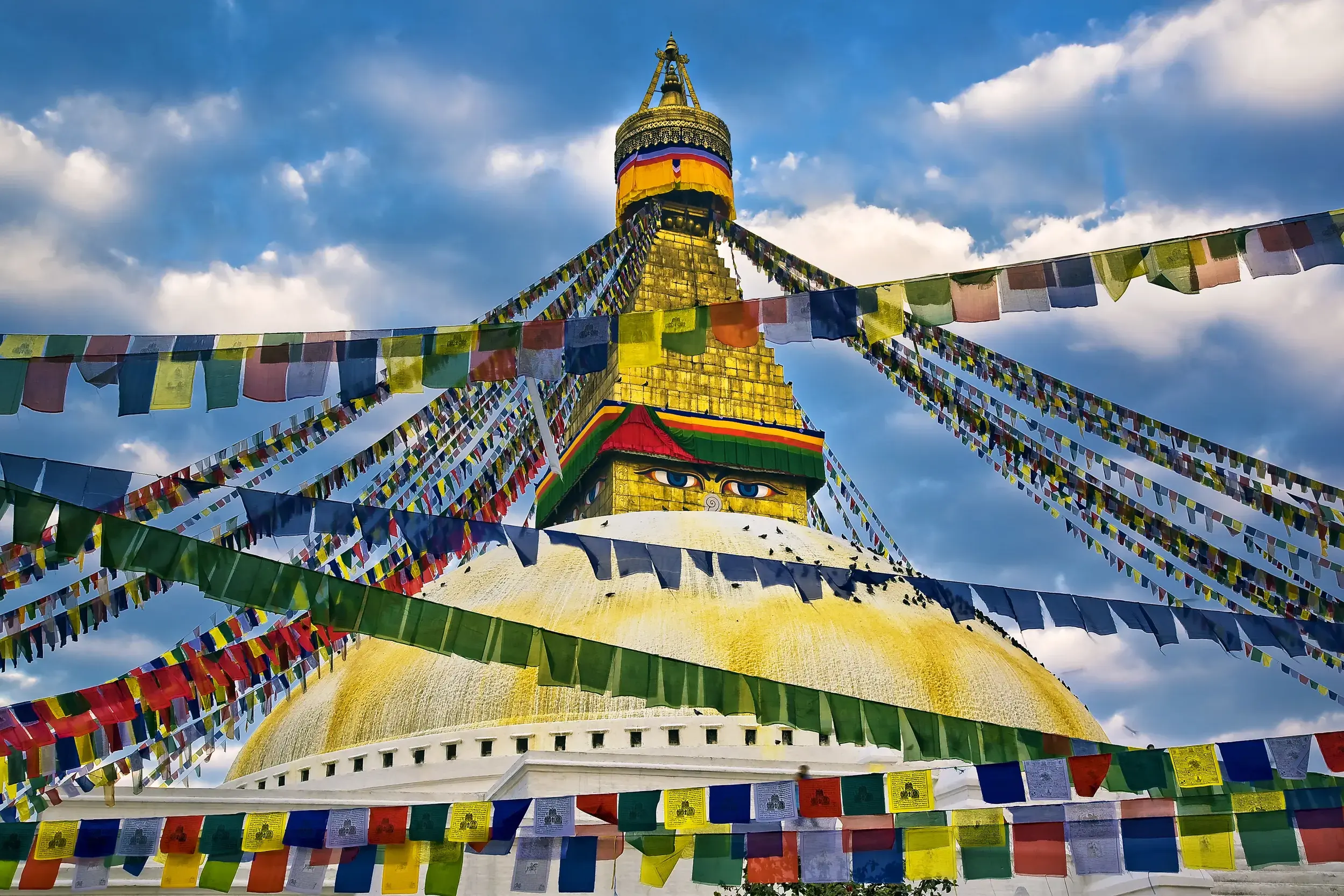 Die majestätische Bodnath Stupa in Kathmandu mit den Augen Buddhas, umgeben von bunten Gebetsfahnen vor blauem Himmel.