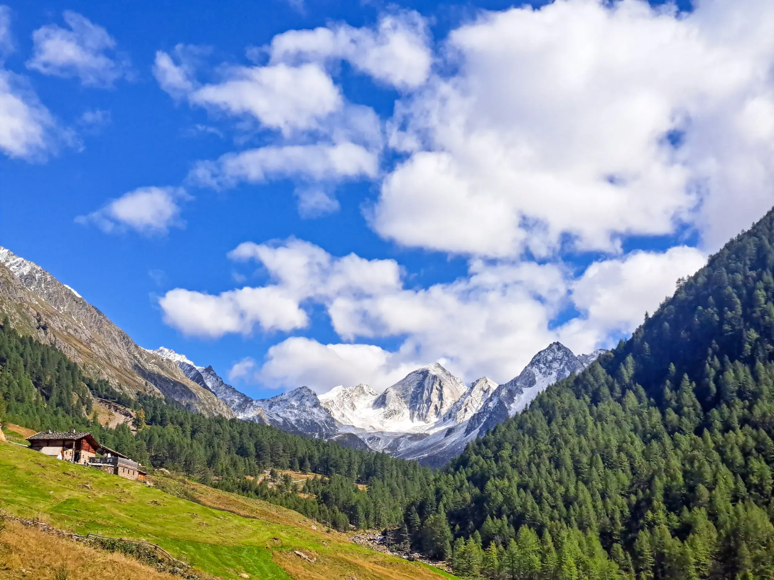Idyllischer Blick in das weite Pfossental mit dem Eishof vor den schneebedeckten Gipfeln der Ötztaler Alpen.