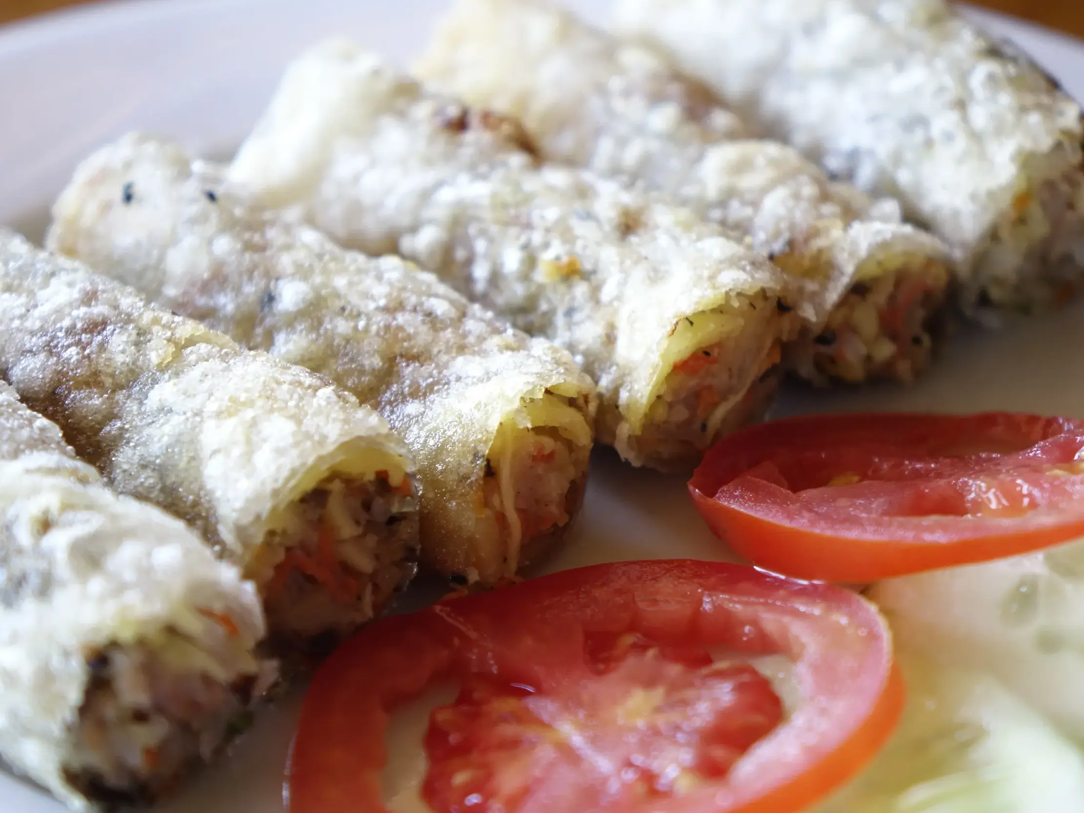 Knusprige, hausgemachte vietnamesische Frühlingsrollen, garniert mit frischen Tomaten auf einem weißen Teller in Südostasien.