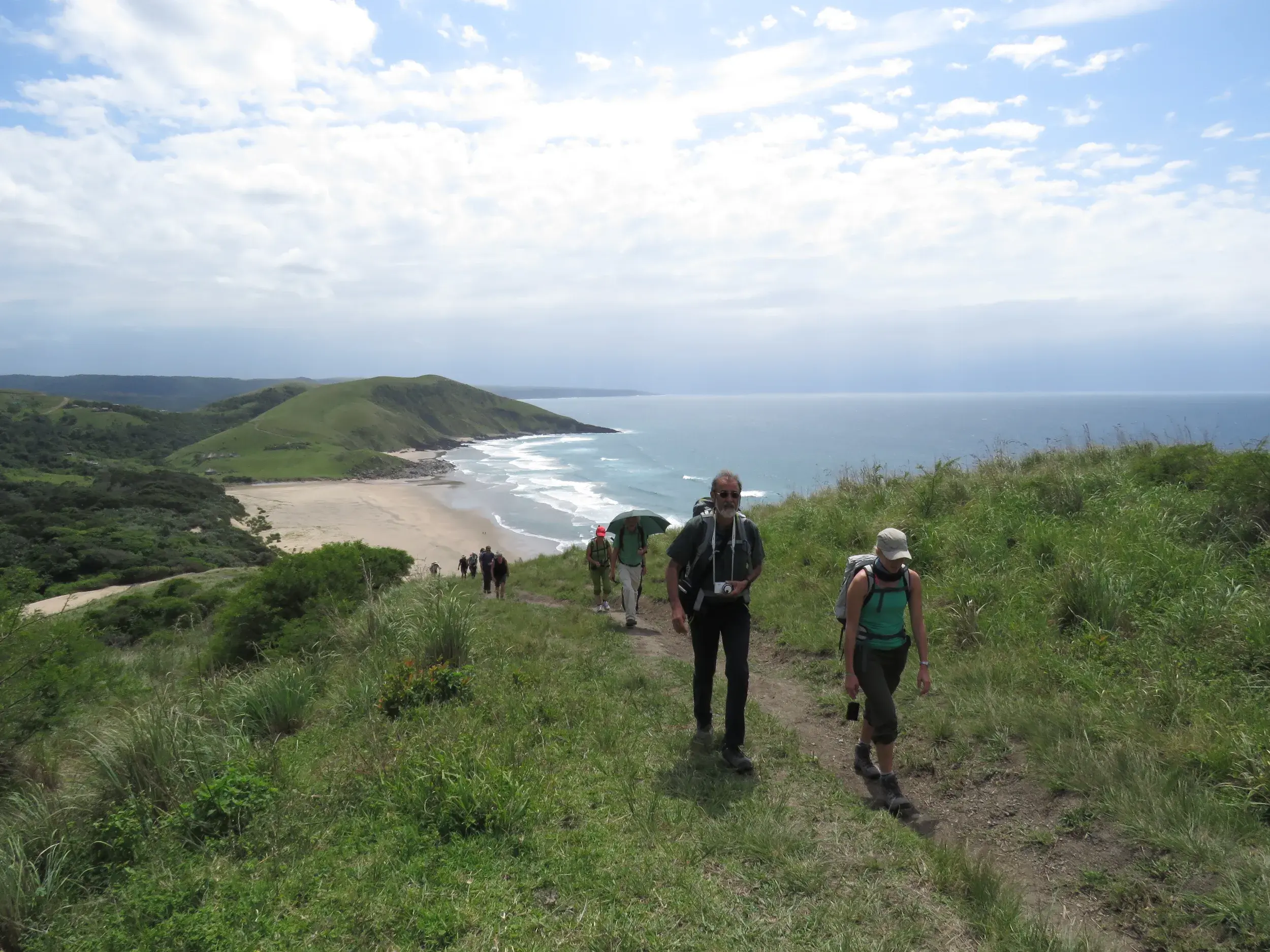 Eine Reisegruppe wandert auf einem Pfad entlang der grünen Hügel der Wild Coast in Südafrika mit Blick aufs Meer.