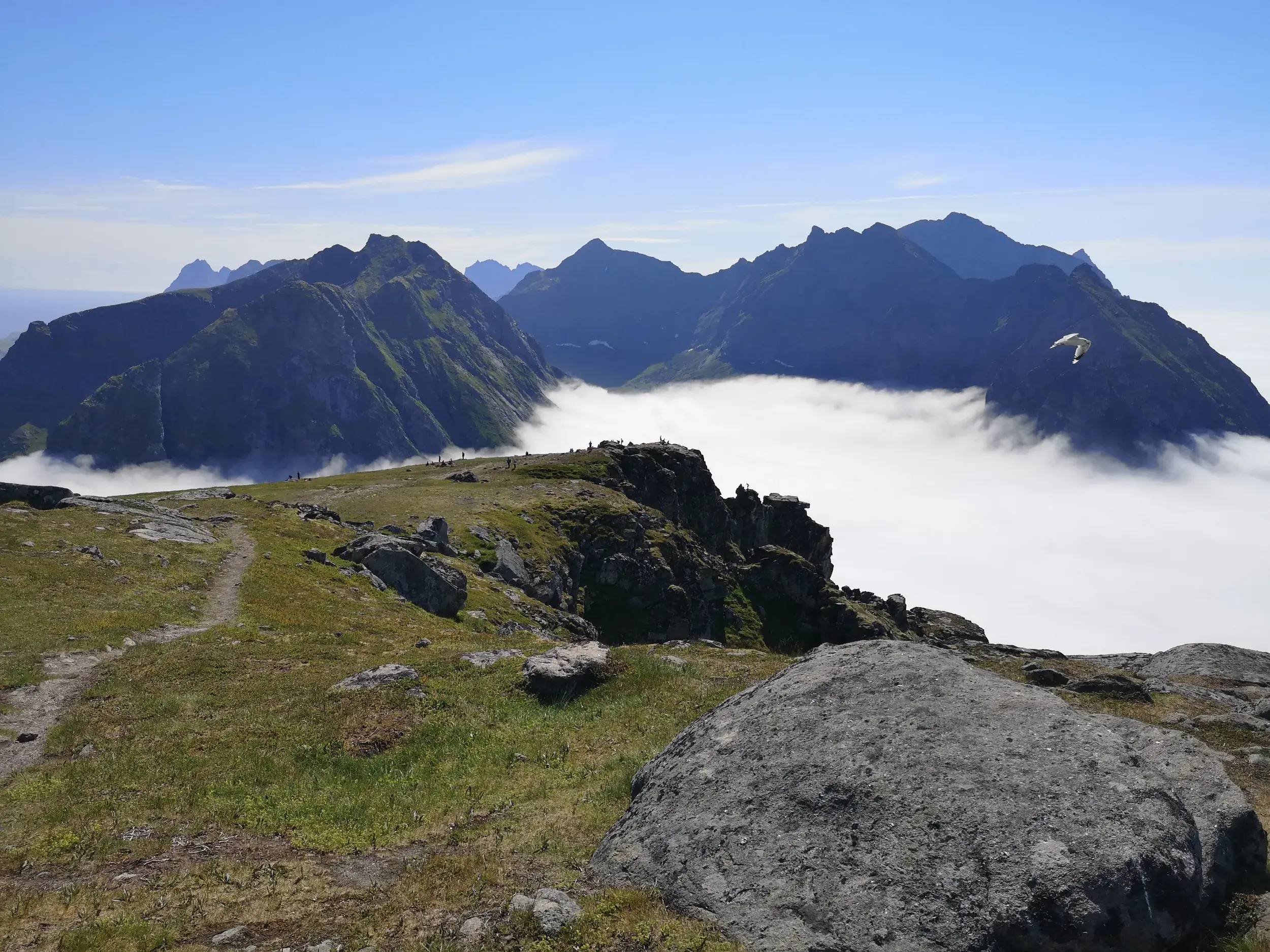 Weite Aussicht vom Gipfel des Ryten auf den Lofoten, wo Wanderer über einem Wolkenmeer auf die zerklüfteten Berge blicken.