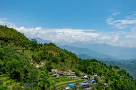 Idyllisches Bergdorf mit grünen Reisterrassen in der Annapurna-Region Nepals vor dem Panorama des Himalaya-Gebirges.