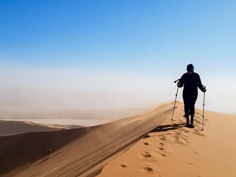 Ein Wanderer mit Trekkingstöcken besteigt den schmalen Grat der riesigen Sanddüne Big Daddy im Sossusvlei, Namibia.