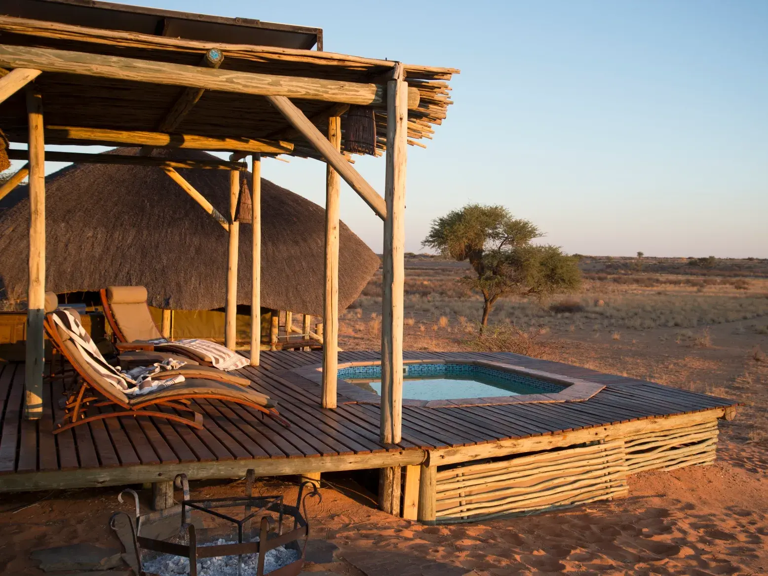Terrasse des luxuriösen Dünen-Camps in der Kalahari mit kleinem Pool und Liegestühlen bei Sonnenuntergang in Namibia.
