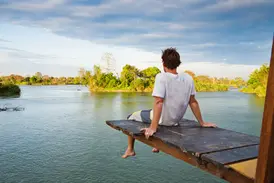 Ein Mann entspannt auf einem Holzsteg über dem Mekong und blickt auf die üppig grüne Flusslandschaft der 4000 Inseln in Laos.