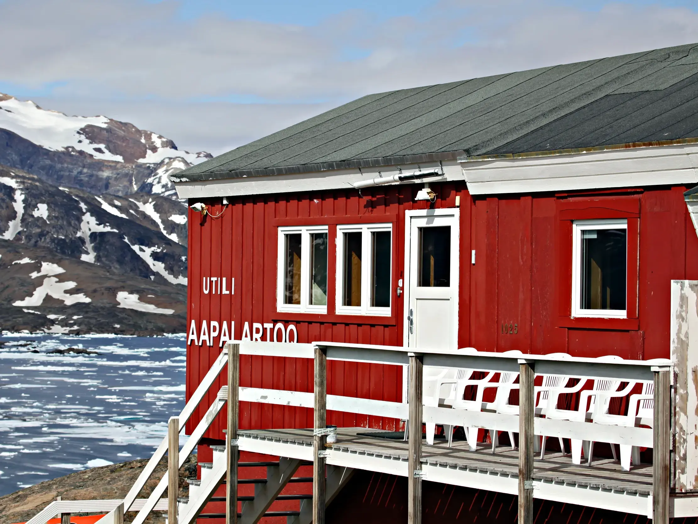 Das rote Gästehaus in Tasiilaq am Ufer des Kong-Oscar-Fjords mit Eisschollen und schneebedeckten Bergen in Ostgrönland.