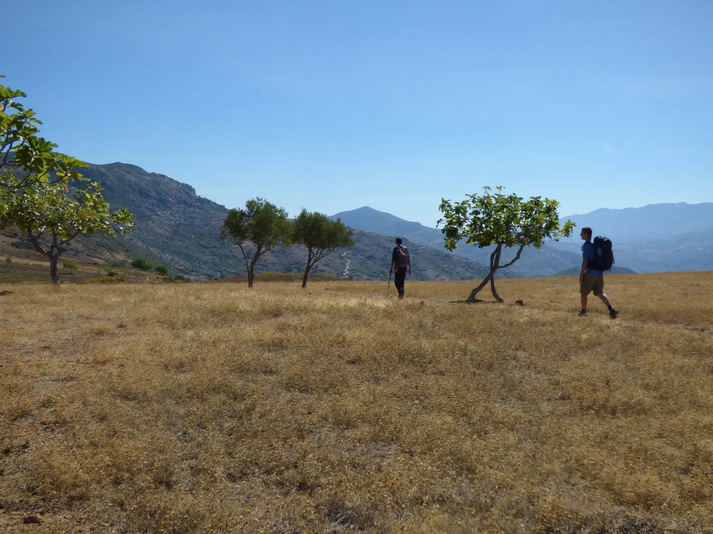 Trekking-Tour in Marokko: Zwei Wanderer durchqueren eine sonnige Hochebene mit Blick auf die Berge des Hohen Atlas.