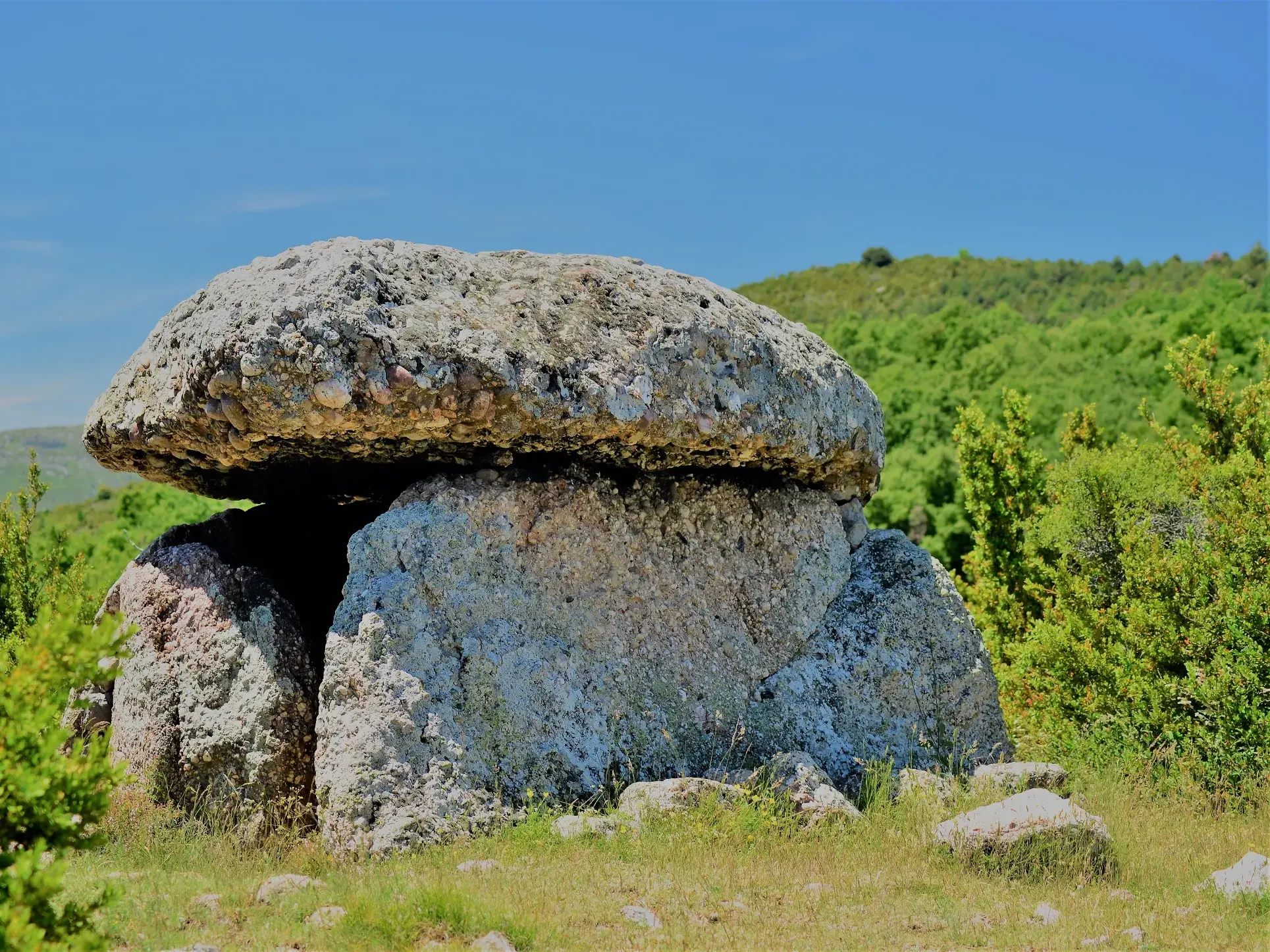 Ein prähistorischer Dolmen aus massiven Felsblöcken in der grünen Hügellandschaft der Vorpyrenäen während einer Trekking-Reise.