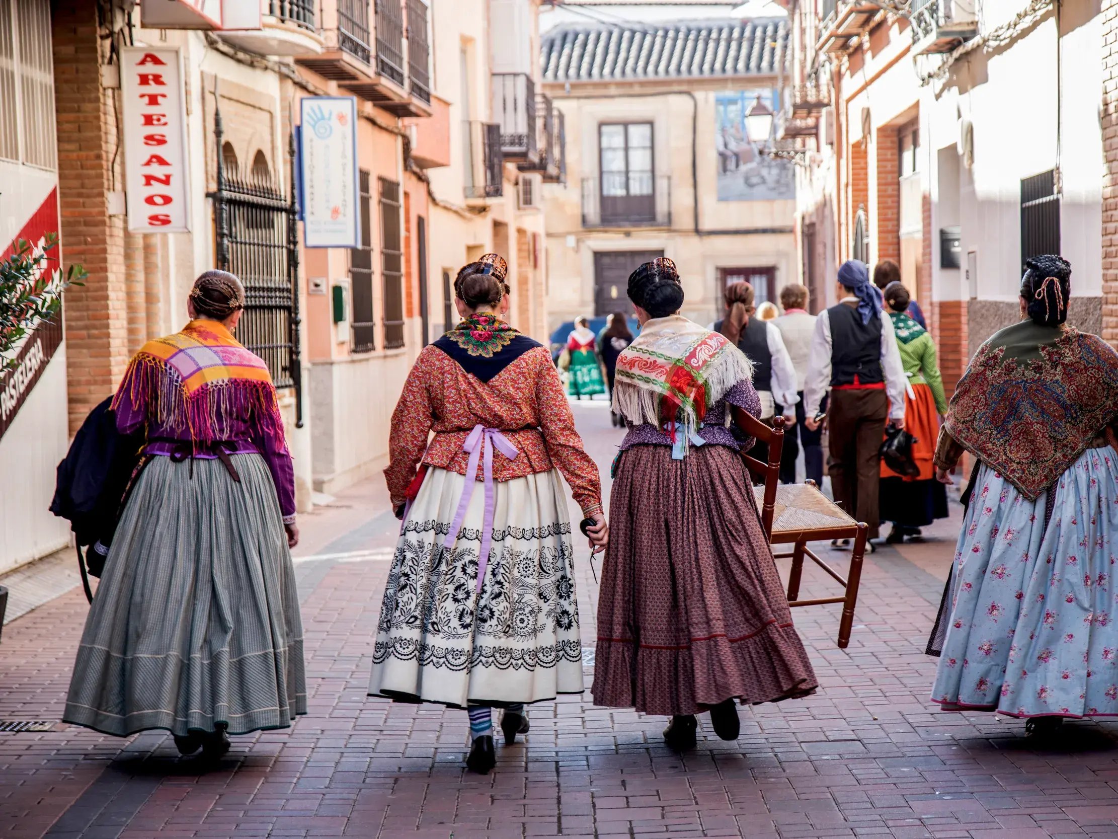Einheimische in farbenfroher, traditioneller kastilischer Tracht spazieren während eines Festumzugs durch eine enge Altstadtgasse.