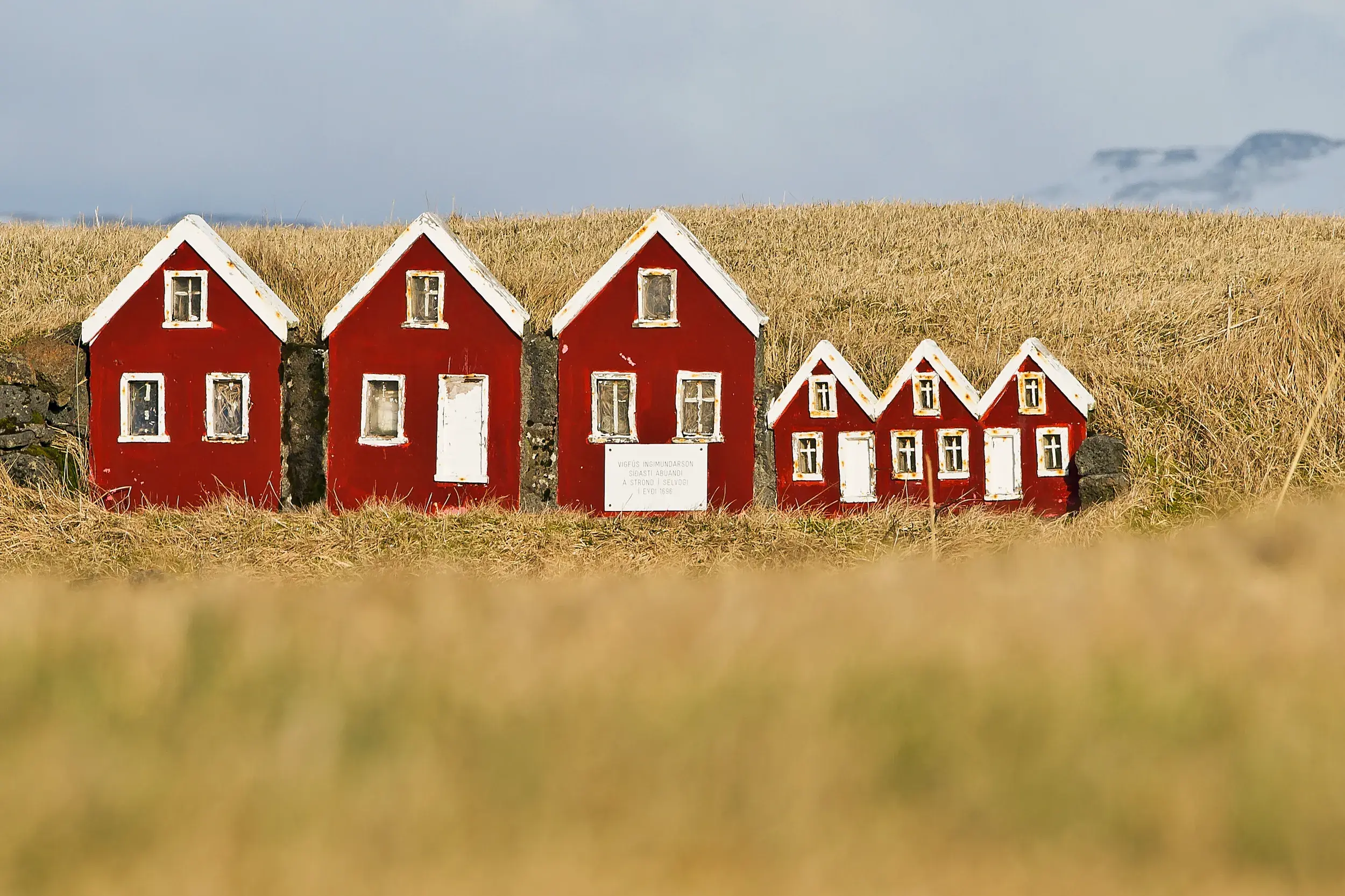 Eine Reihe roter Miniatur-Häuser für die Weihnachtsmänner bei Dimmuborgir, eingebettet in einen grasbewachsenen Wall.