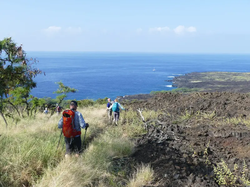 Wandergruppe auf einem Trekkingpfad an der Küste von Hawaii mit Blick über erkaltete Lavafelder auf den Pazifischen Ozean.