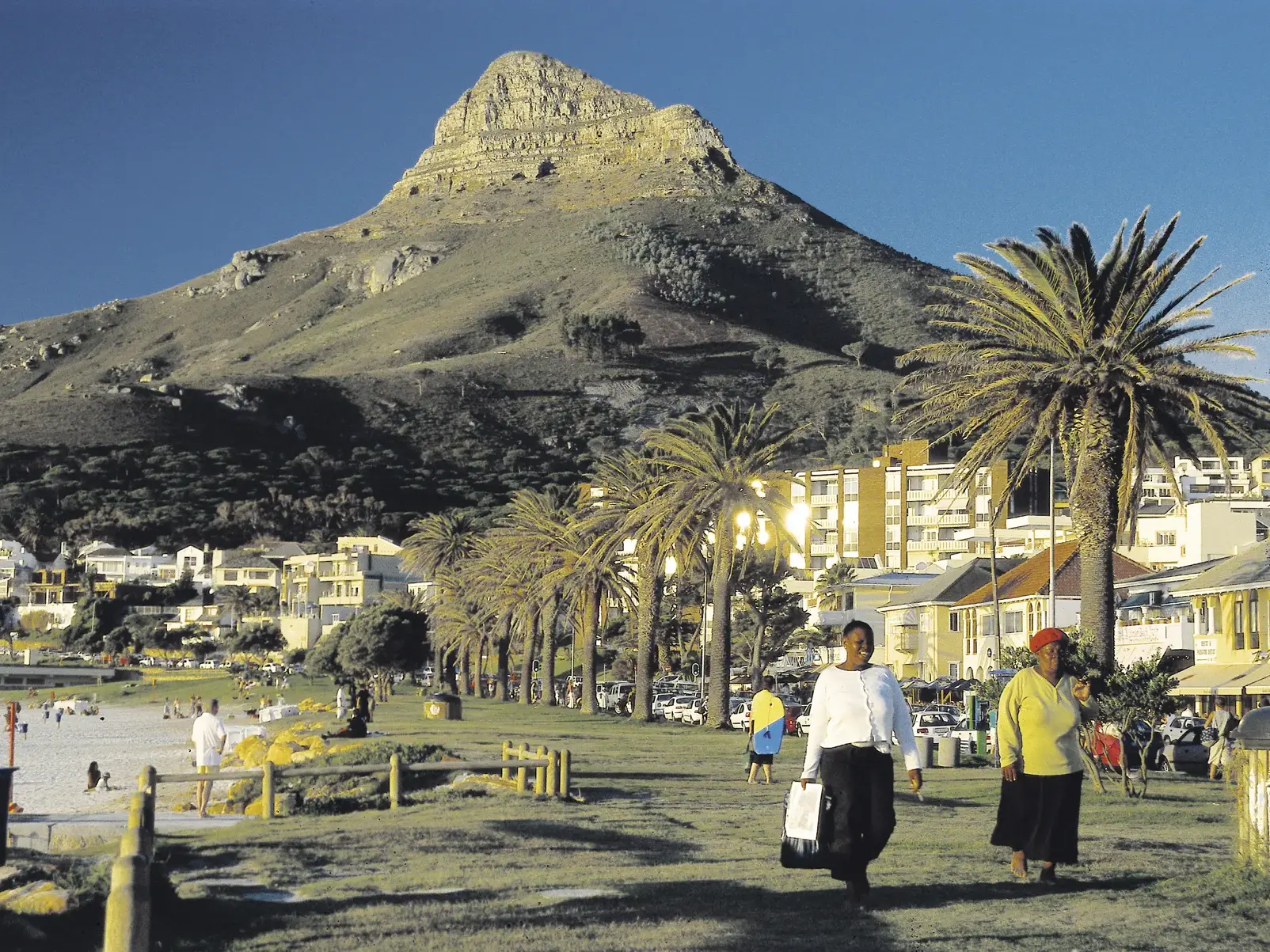 Einheimische spazieren an der palmengesäumten Promenade von Kapstadt, während der Lion's Head in der Abendsonne erstrahlt.