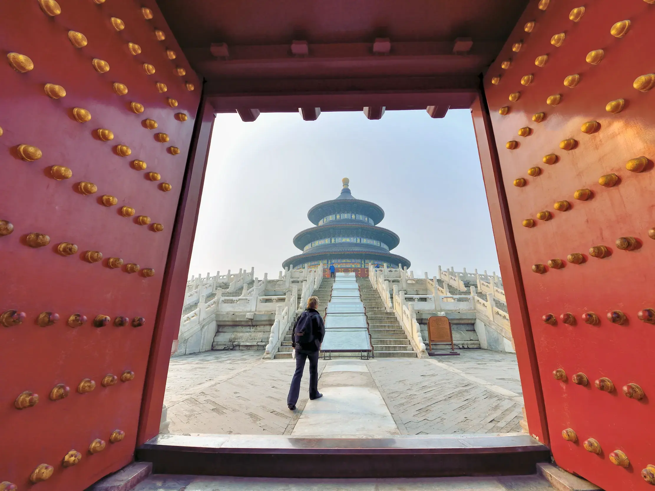 Ein Reisender auf einer geführten Rundreise blickt durch ein rotes Tor auf die Halle des Erntegebets im Himmelstempel in Peking.