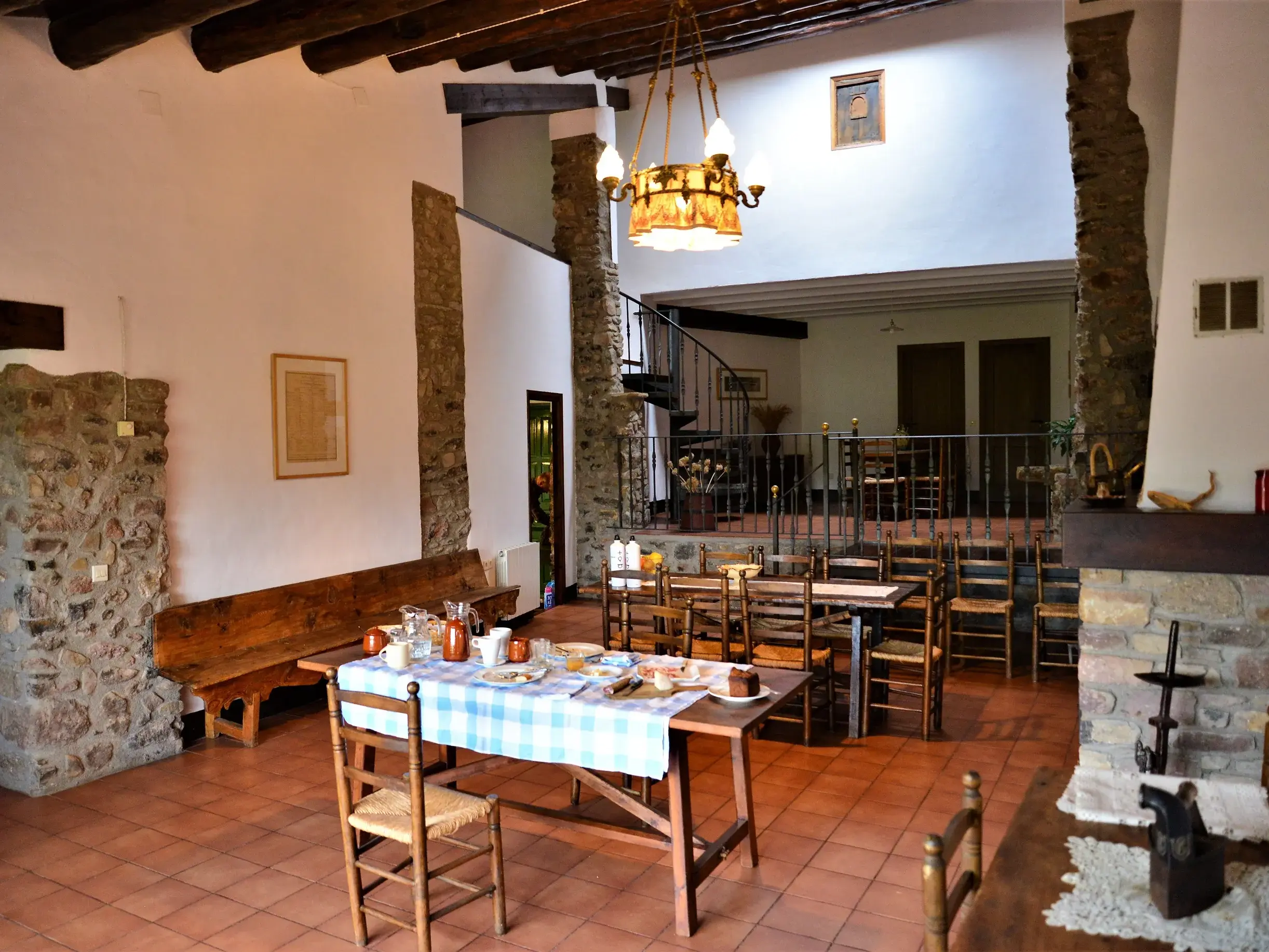 Gedeckter Frühstückstisch im Essbereich eines rustikalen Gästehauses in den Pyrenäen mit Steinpfeilern und Wendeltreppe.