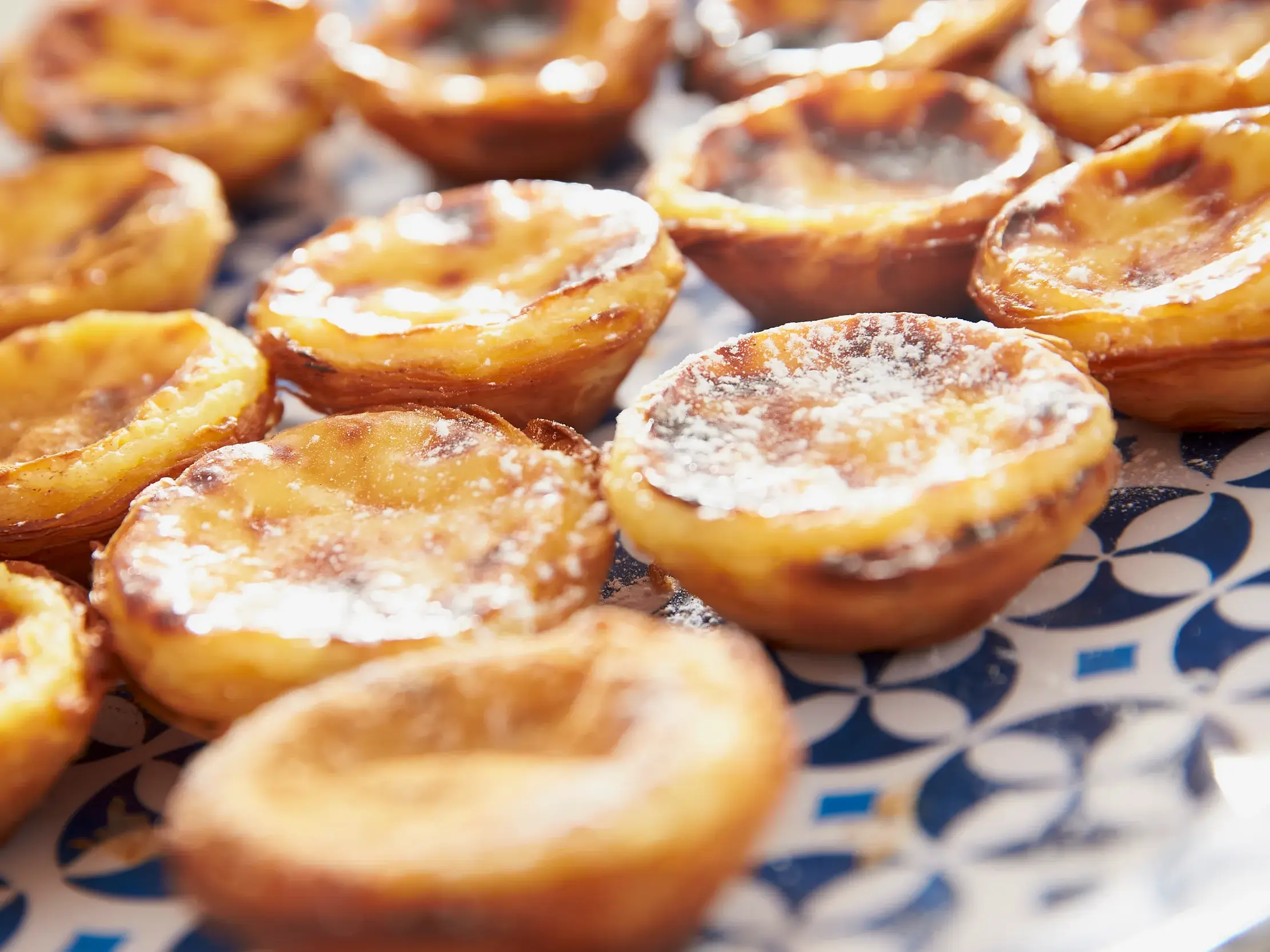 Frische Pastéis de Nata mit Puderzucker auf einer Platte als kulinarische Probe bei einer Marco Polo Rundreise in Lissabon.
