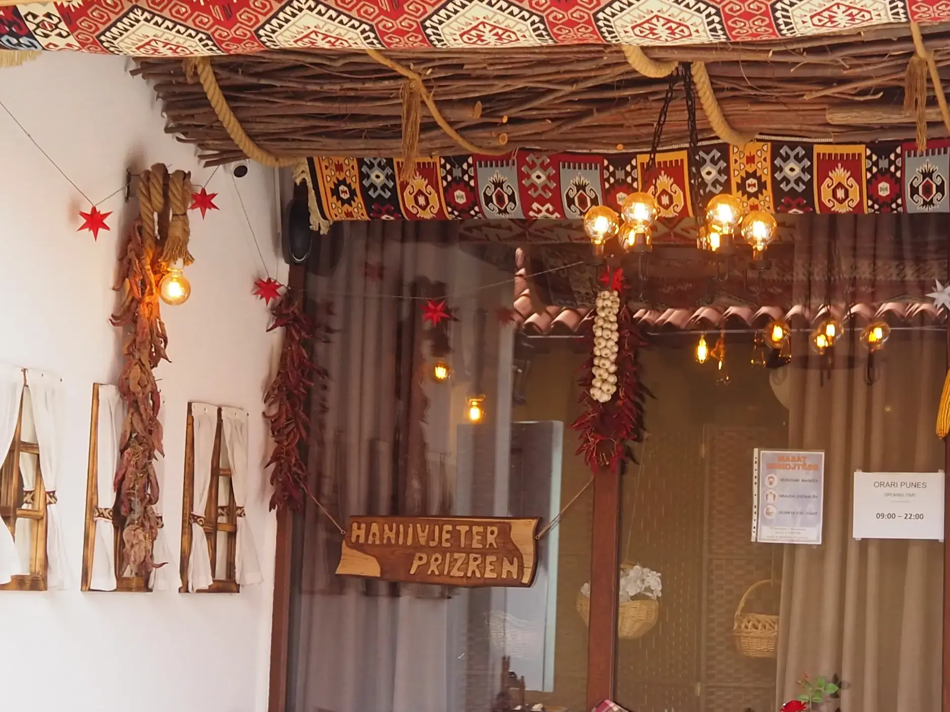 Eingang des traditionellen Gasthauses Hani i Vjeter in Prizren, Kosovo, mit rustikaler Deko aus Teppichen und Chilischoten.