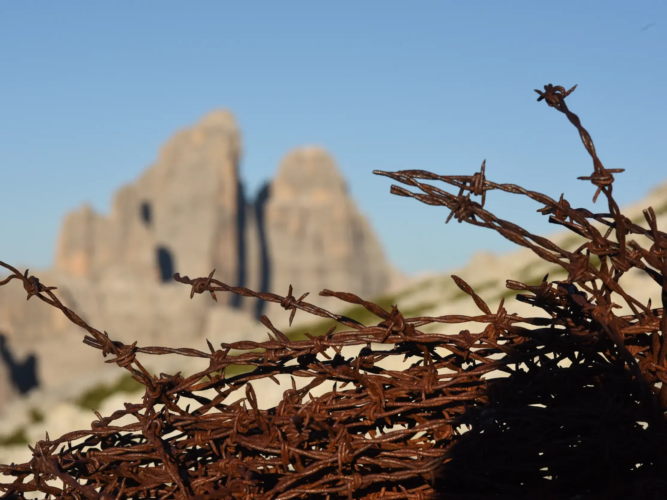 Rostiger Stacheldraht aus dem Ersten Weltkrieg vor den Felszacken der Drei Zinnen in den Dolomiten bei Sonnenschein.