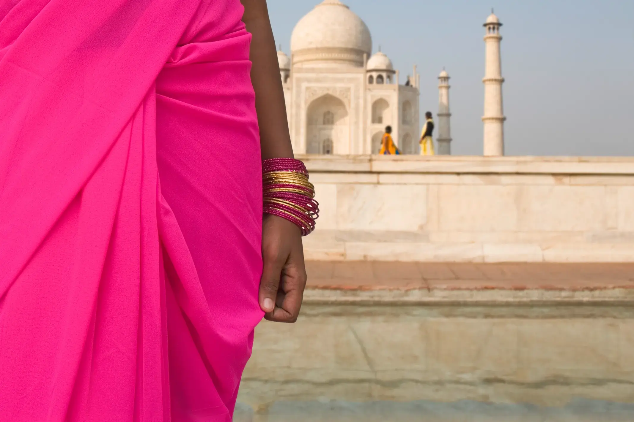 Eine Frau in einem leuchtend pinken Sari und goldenen Armreifen blickt auf das weltberühmte Taj Mahal in Agra, Indien.