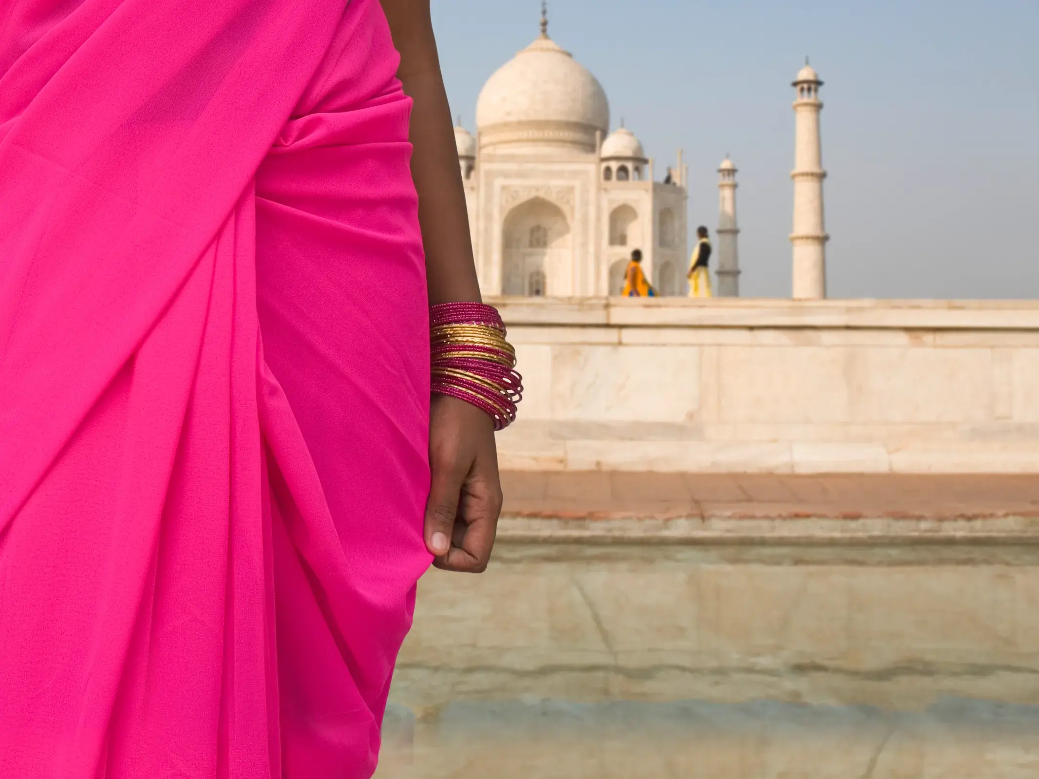 Eine Frau in einem leuchtend pinken Sari und goldenen Armreifen blickt auf das weltberühmte Taj Mahal in Agra, Indien.