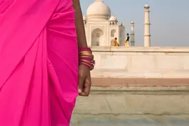Eine Frau in einem leuchtend pinken Sari und goldenen Armreifen blickt auf das weltberühmte Taj Mahal in Agra, Indien.