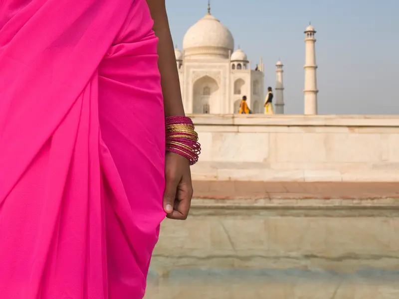 Eine Frau in einem leuchtend pinken Sari und goldenen Armreifen blickt auf das weltberühmte Taj Mahal in Agra, Indien.