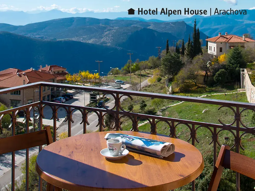 Balkon mit Tisch und Kaffee im Hotel Alpen House mit Blick auf das Bergdorf Arachova und das weite Parnassgebirge am Morgen.
