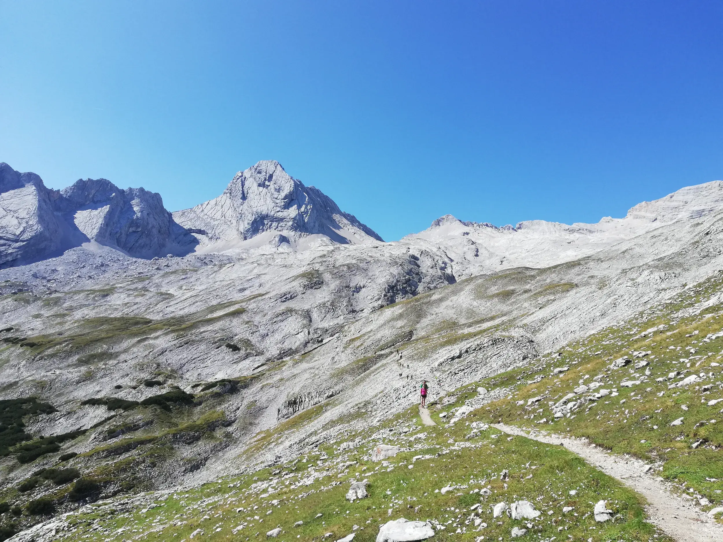 Eine Wandergruppe auf einem schmalen Bergpfad während einer Alpenüberquerung durch die hochalpine Felslandschaft Tirols.