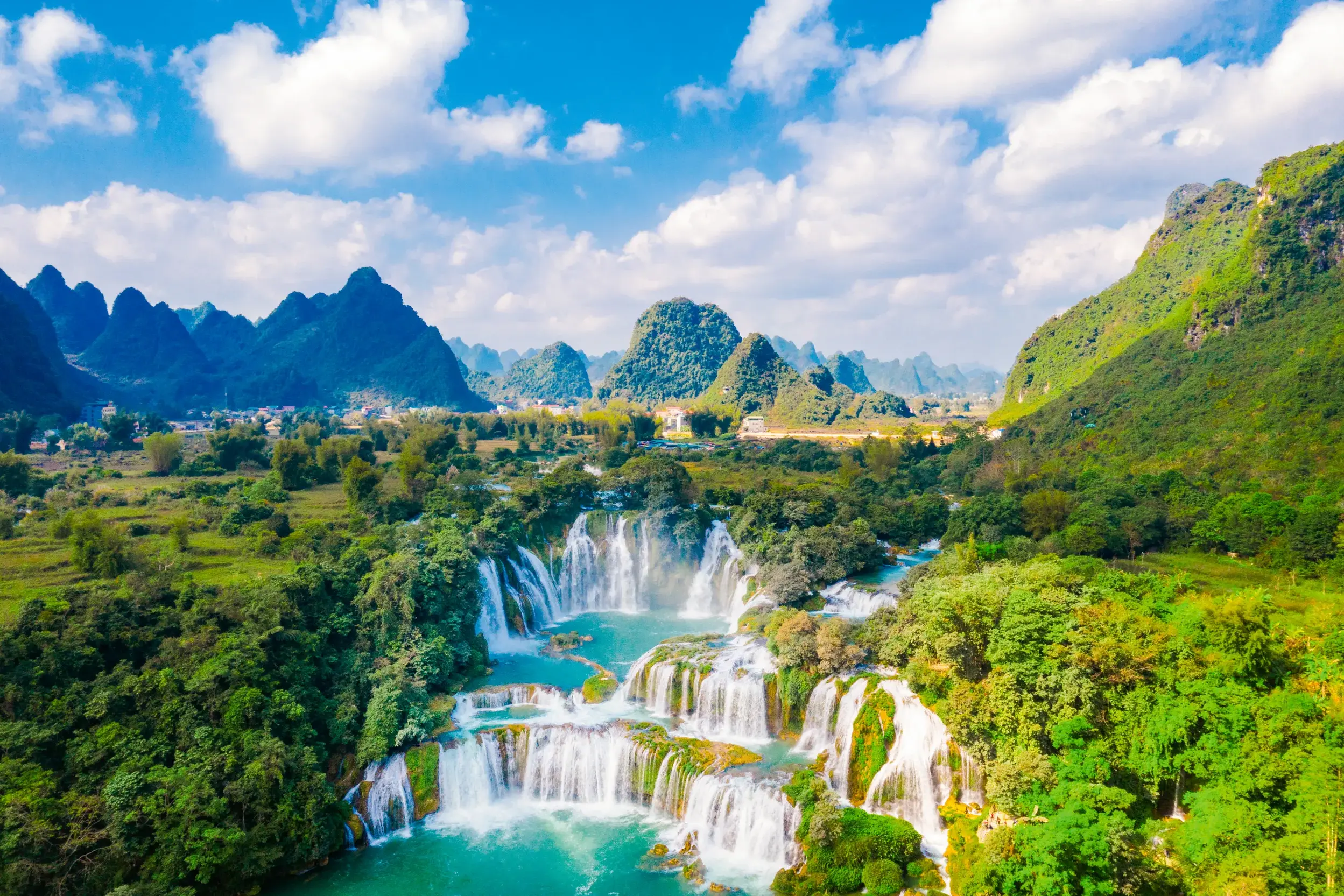 Die beeindruckenden Ban-Gioc Wasserfälle in Nordvietnam, umgeben von grünen Karstbergen und üppigem Dschungel.