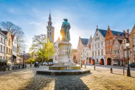 Historischer Jan-van-Eyck-Platz in Brügge mit Giebelhäusern und der Statue des Malers im goldenen Licht der Morgensonne.