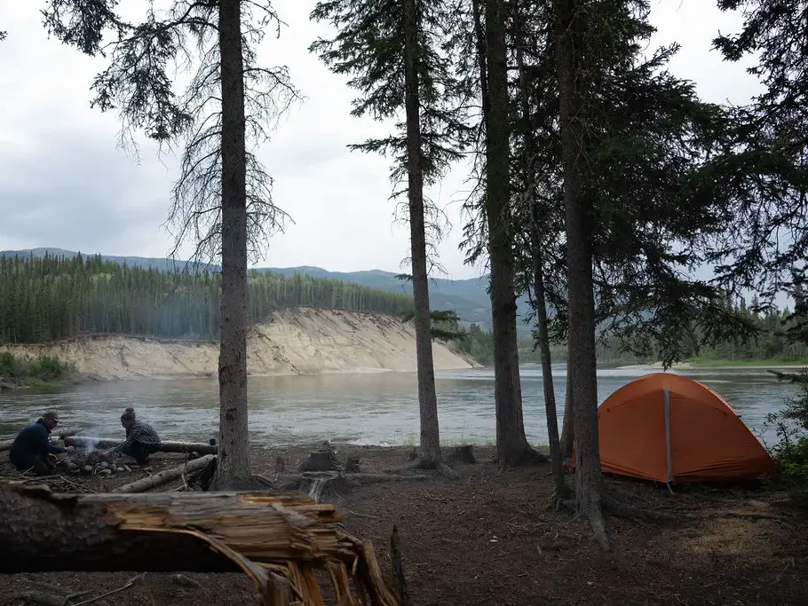 Zeltlager mit Lagerfeuer am Ufer des Yukon River während einer Kanutrekking-Reise in der kanadischen Wildnis.