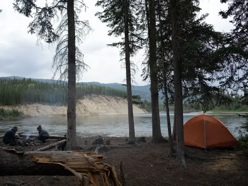 Zeltlager mit Lagerfeuer am Ufer des Yukon River während einer Kanutrekking-Reise in der kanadischen Wildnis.