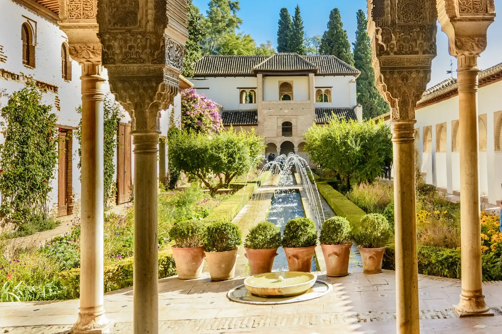 Maurische Torbögen mit filigranen Arabesken umrahmen den Blick auf einen sonnigen Innenhof der Alhambra in Granada.