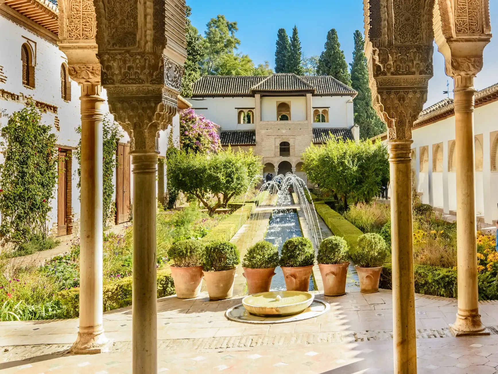 Maurische Torbögen mit filigranen Arabesken umrahmen den Blick auf einen sonnigen Innenhof der Alhambra in Granada.