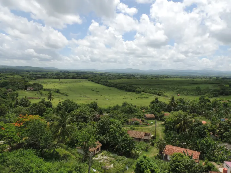Weitblick über die hügelige, grüne Landschaft im ländlichen Kuba mit kleinen Bauernhäusern und tropischer Vegetation.