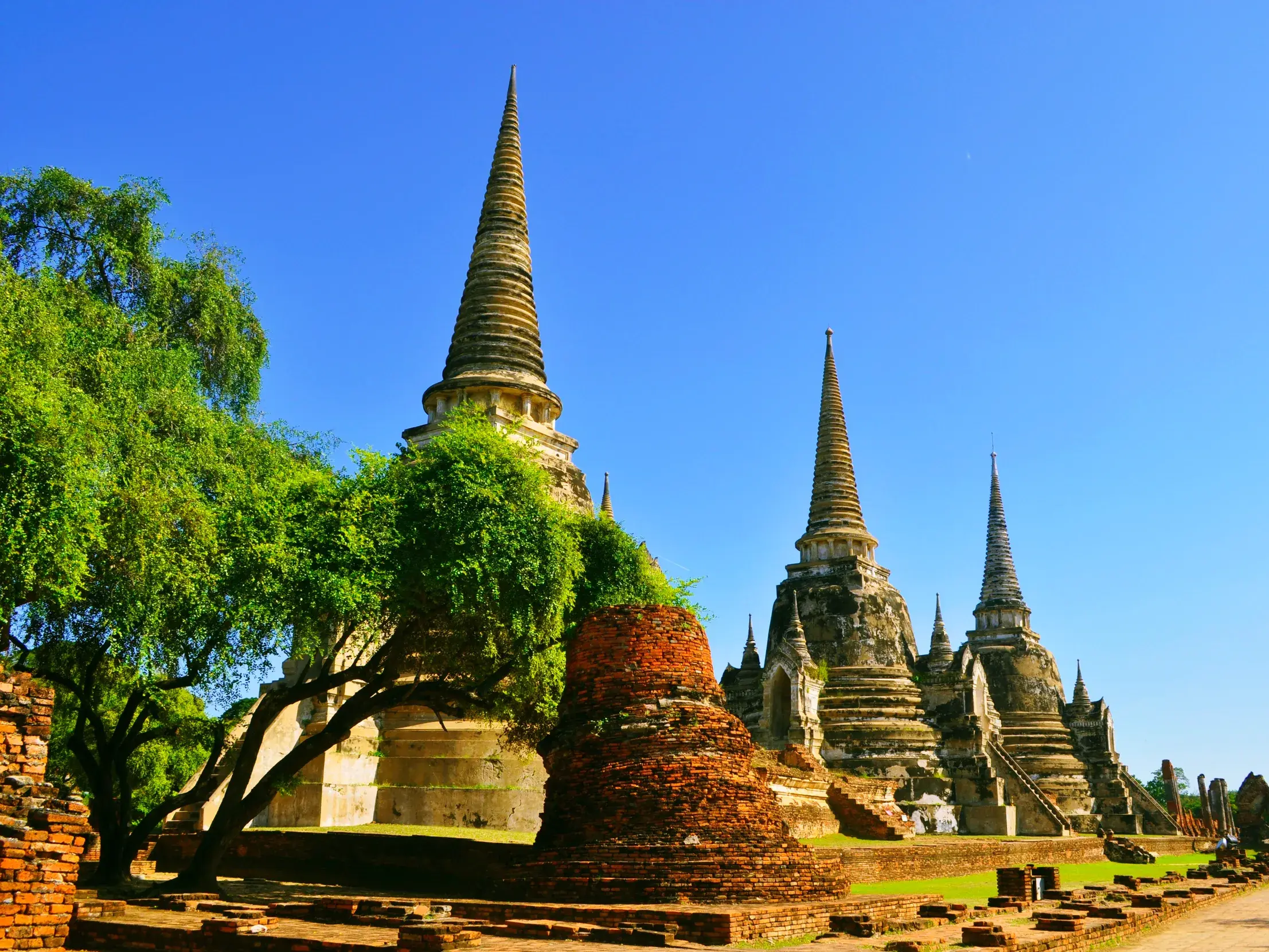Steinerne Chedis der historischen Tempelanlage von Ayutthaya in Thailand ragen bei Sonnenschein in den tiefblauen Himmel.