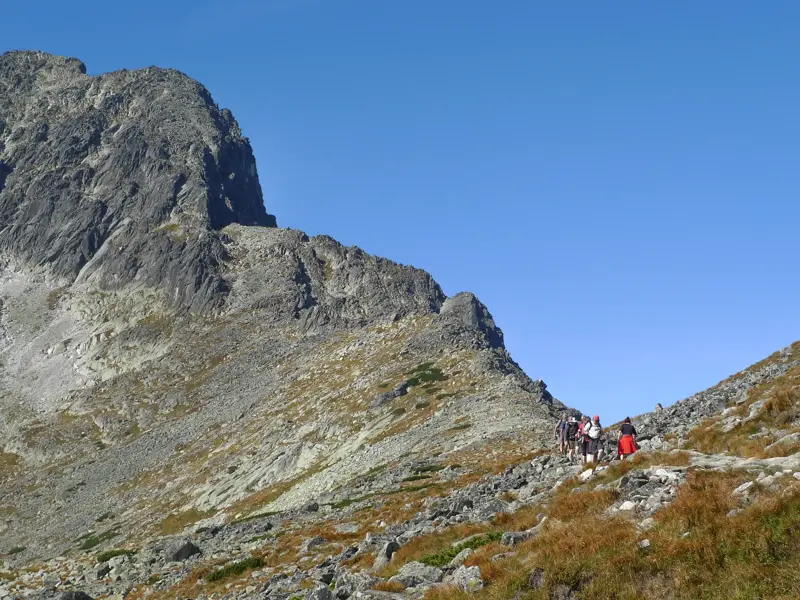 Wandergruppe beim Trekking auf der Tatranska Magistrale in der Hohen Tatra vor einem schroffen, felsigen Berggipfel.