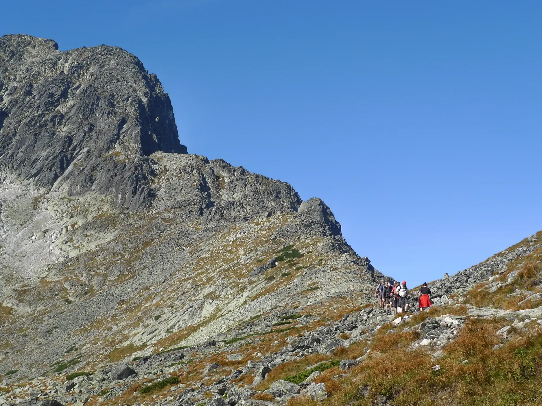 Eine Trekkinggruppe wandert auf dem felsigen Höhenweg Tatranska Magistrale unterhalb des Berggipfels Łomnicki in der Hohen Tatra.