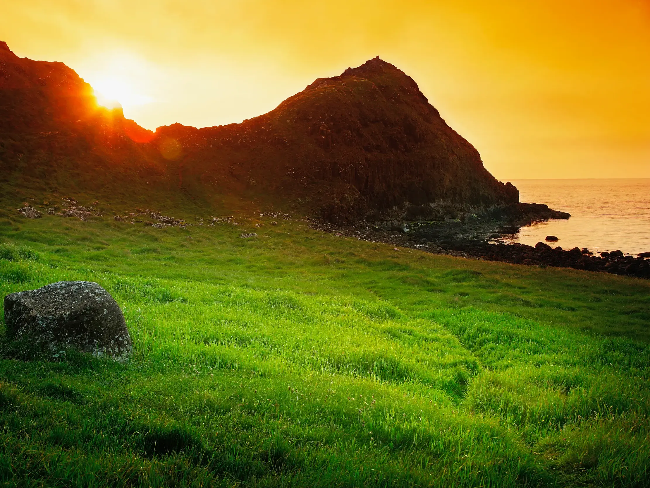 Die untergehende Sonne taucht die Felsenküste am Giant's Causeway in Nordirland in ein warmes, goldenes Abendlicht.