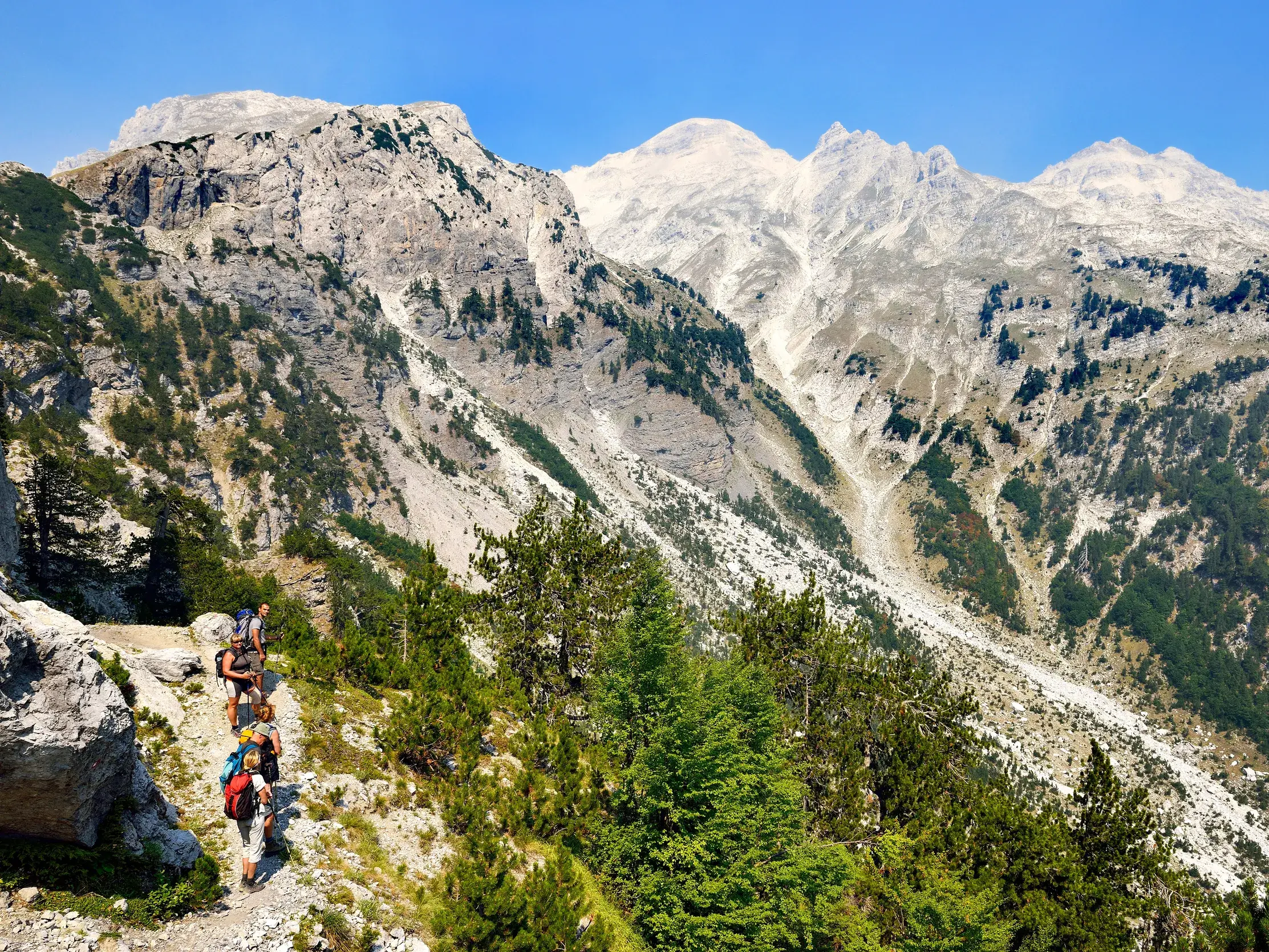 Eine Wandergruppe auf dem 'Peaks of the Balkans'-Trail mit Blick auf die schroffen, hellen Gipfel der Albanischen Alpen.