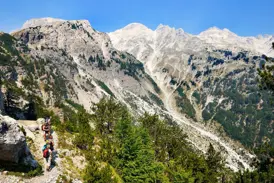 Eine Wandergruppe auf dem 'Peaks of the Balkans'-Trail mit Blick auf die schroffen, hellen Gipfel der Albanischen Alpen.