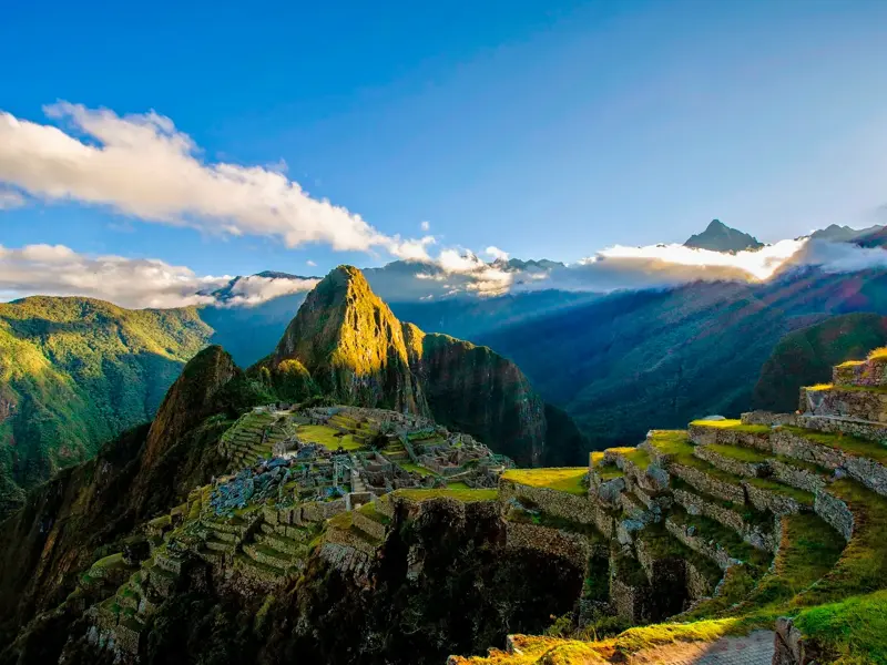 Die Inkastadt Machu Picchu in den peruanischen Anden, beleuchtet von der goldenen Morgensonne unter einem blauen Himmel.