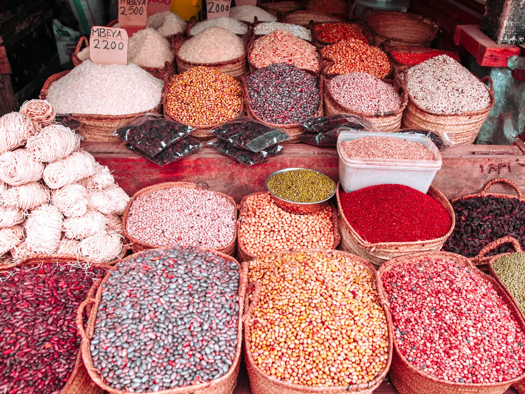 Bunte Hülsenfrüchte, Reis und Gewürze in geflochtenen Körben auf einem lokalen Marktstand in Tansania mit Preisschildern.