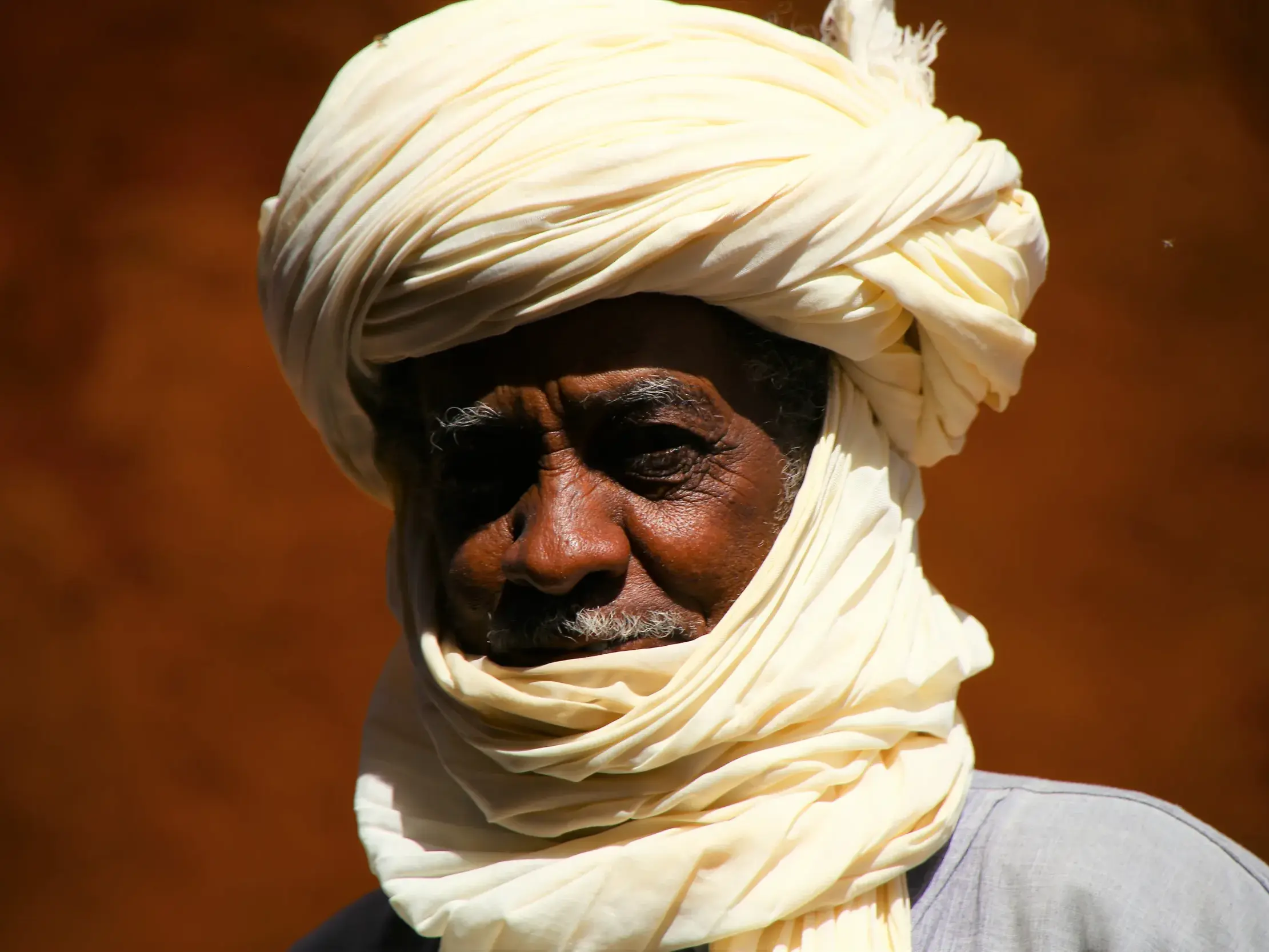 Porträt eines erfahrenen Tuareg-Reiseleiters mit Turban, sein von der Sonne der Sahara gezeichnetes Gesicht nachdenklich.