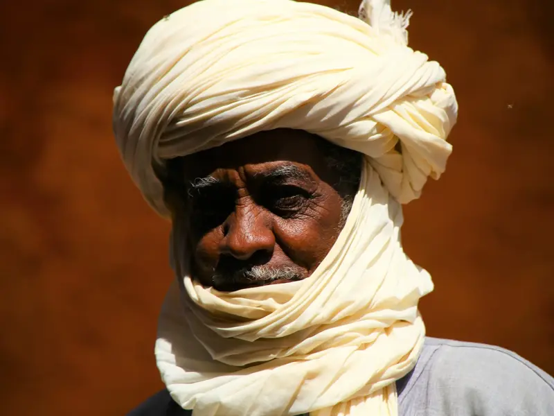Porträt eines erfahrenen Tuareg-Reiseleiters mit Turban, sein von der Sonne der Sahara gezeichnetes Gesicht nachdenklich.