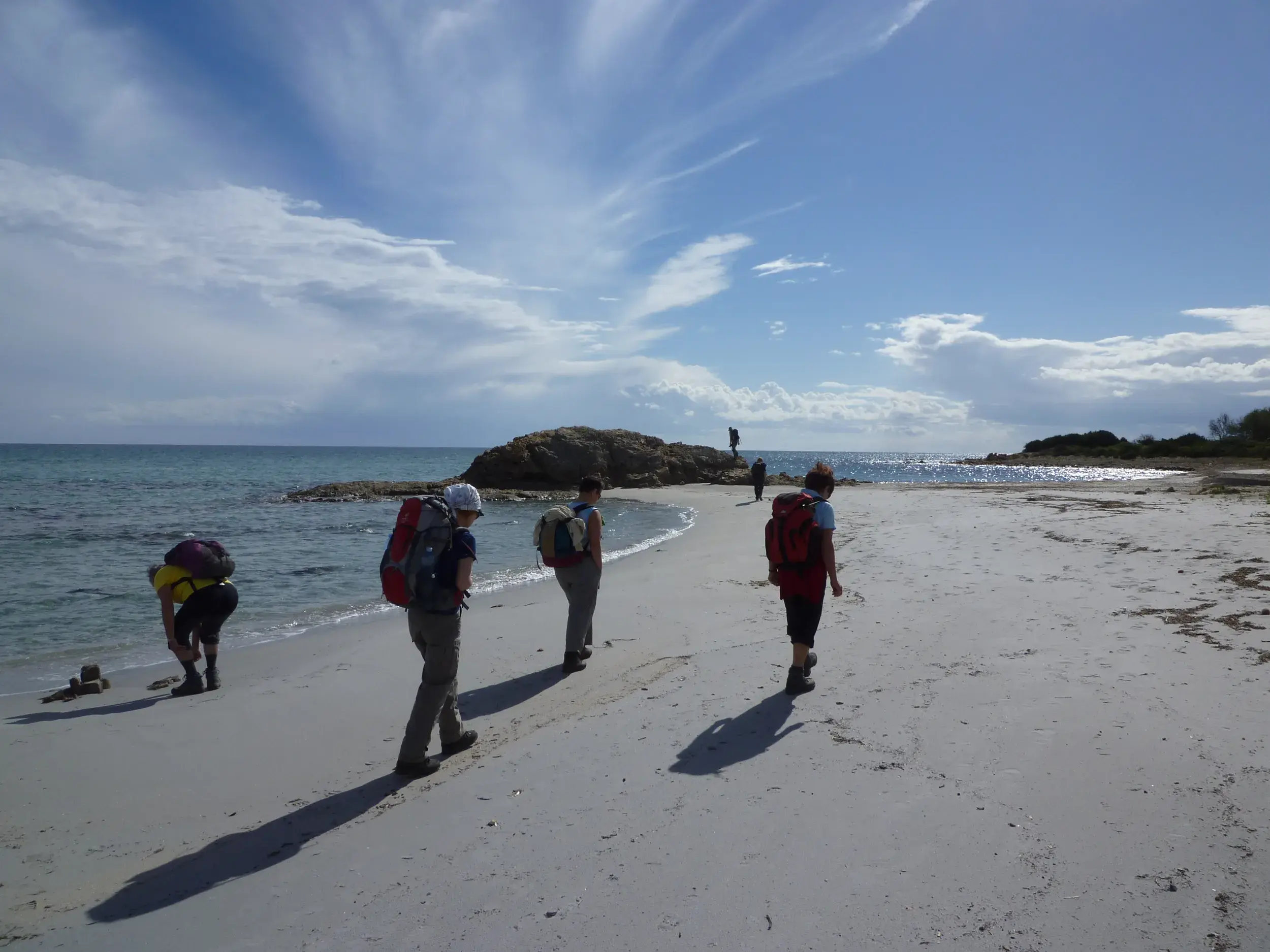 Eine Hauser-Wandergruppe mit Trekkingrucksäcken wandert am weiten Sandstrand der Halbinsel Sinis auf Sardinien.